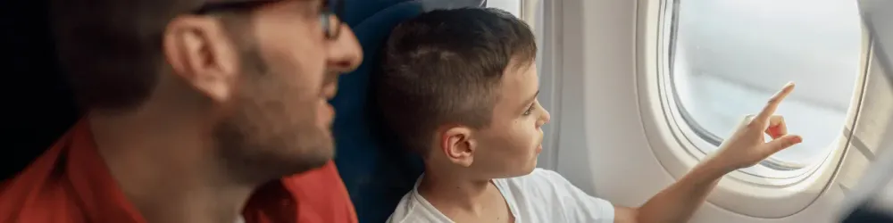 Curious little boy looking out the window while traveling by plane together with his father. Family, transportation, vacation concept